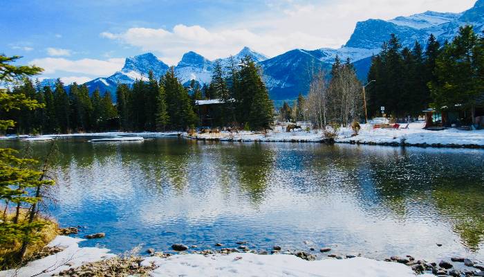 A photo of a pond in Canmore, AB, Canada, with snow, elk, and mountains in the background. A great place for nature therapy!