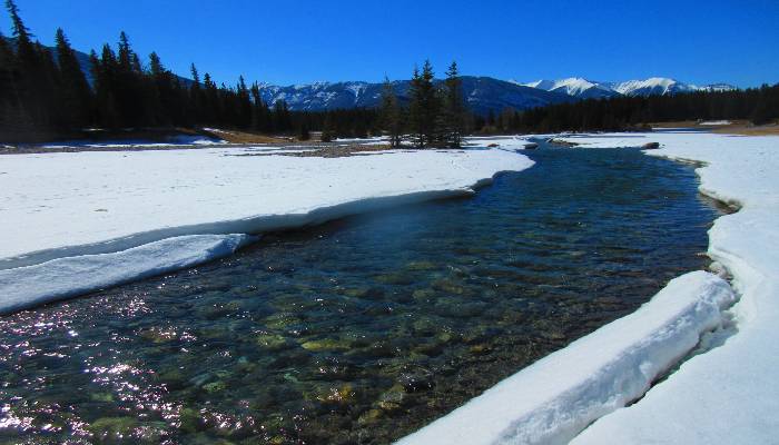 A photo of snow melting along a river of water at Cascade in Banff, Alberta, Canada. We learn how to manifest by observing nature. Like the rushing water, we are filled with a rush of new energy in Spring that allows us to create and manifest.