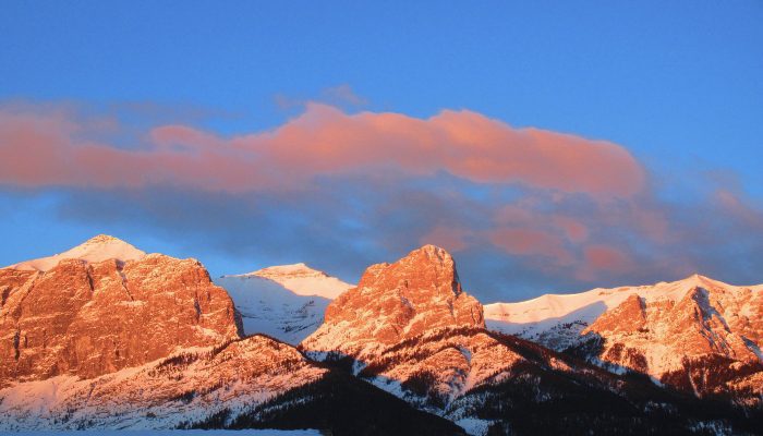 A photo of pink cotton-candy clouds, and blue sky on a sunrise morning over the mountains in Canmore, Alberta, Canada. Looks like divine love, and here's how we can experience more of it.