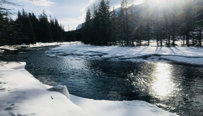 A photo of Spray River in Banff, Alberta Canada with snow, ice, and sun reflecting off the flowing water. We can manifest what we want when we move with ease and flow like the river with these manifesation methods.