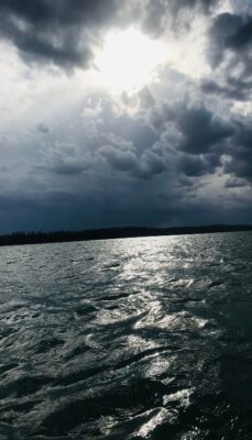 A photo of an ominous looking dark sky with sun shining through over some wavy waters like overcoming obstacles requires movement through waves and dark skies sometimes.